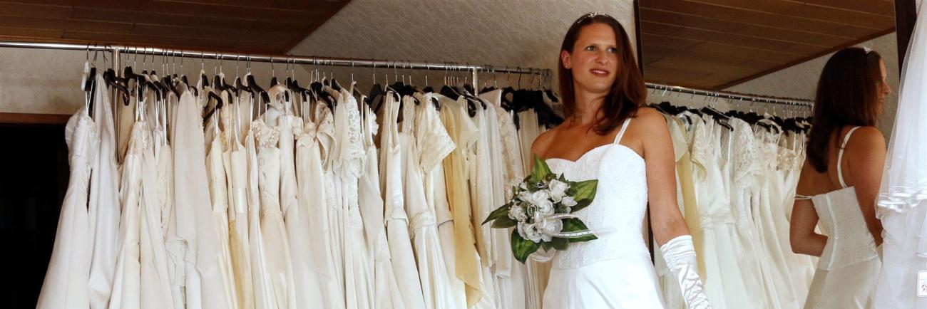 Eine Frau in einem weißen Brautkleid in einem Geschäft voller Hochzeitskleider.