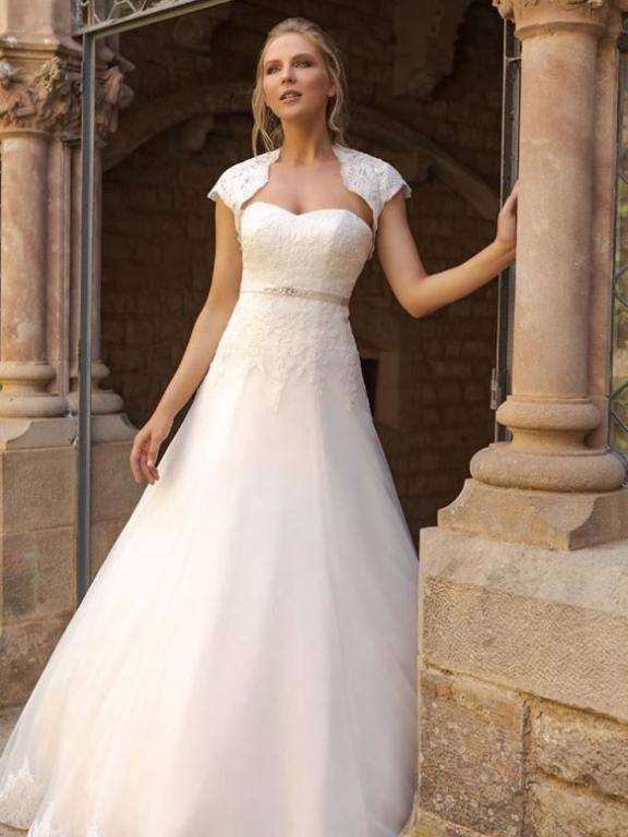 Eine Frau in einem weißen Hochzeitskleid steht vor einem historischen steinernen Fenster und Säule.