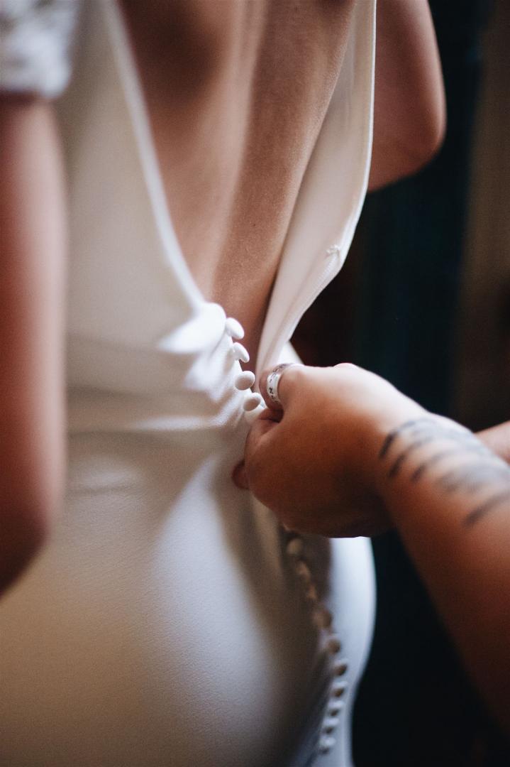 Nahaufnahme eines schwangeren Bauches, der in einem hellen Kleid sichtbar ist und von einer Hand gehalten wird.