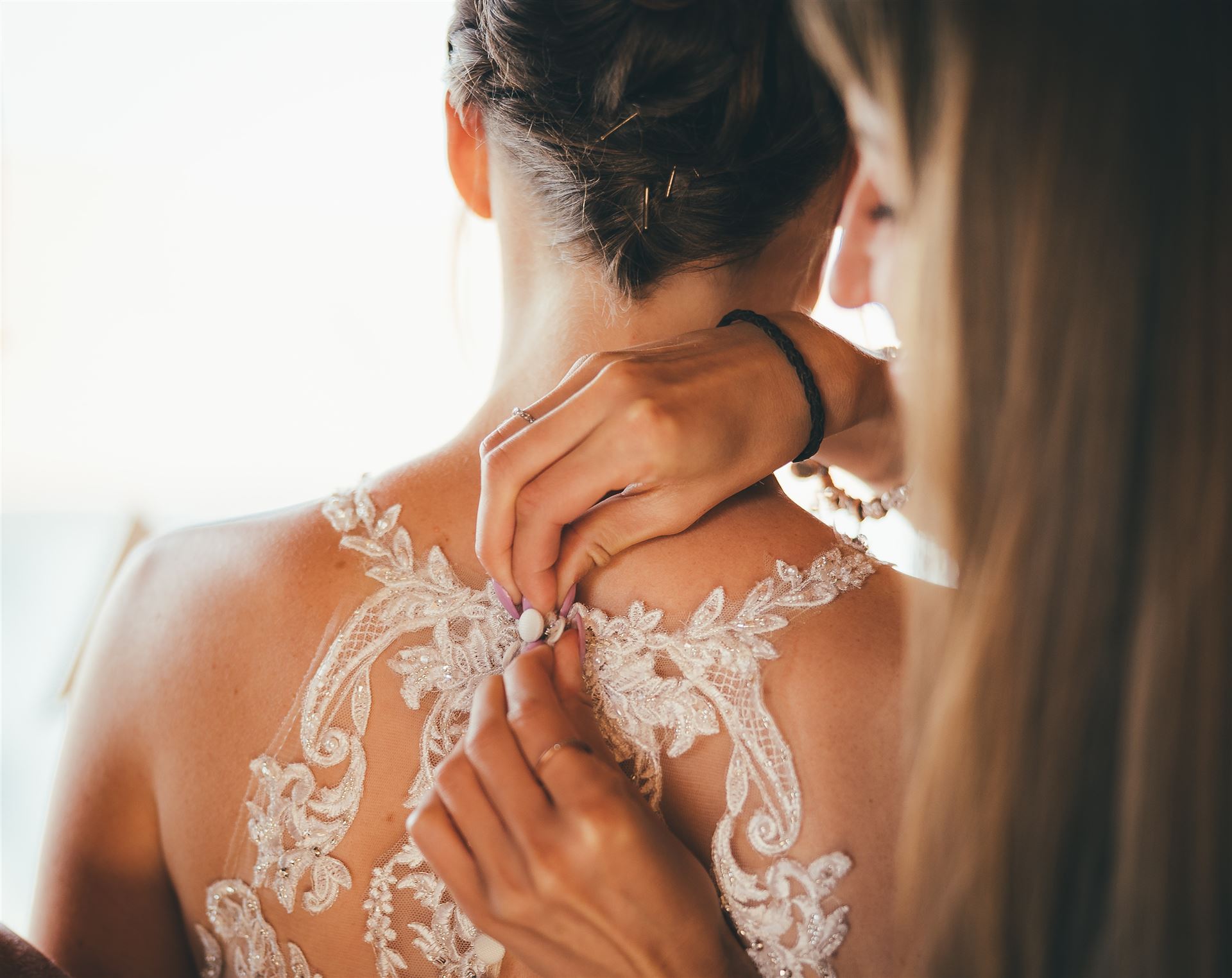 Zwei Frauen in engem Kontakt; eine trägt ein filziges Spitzenkleid und wird von der anderen Person berührt.