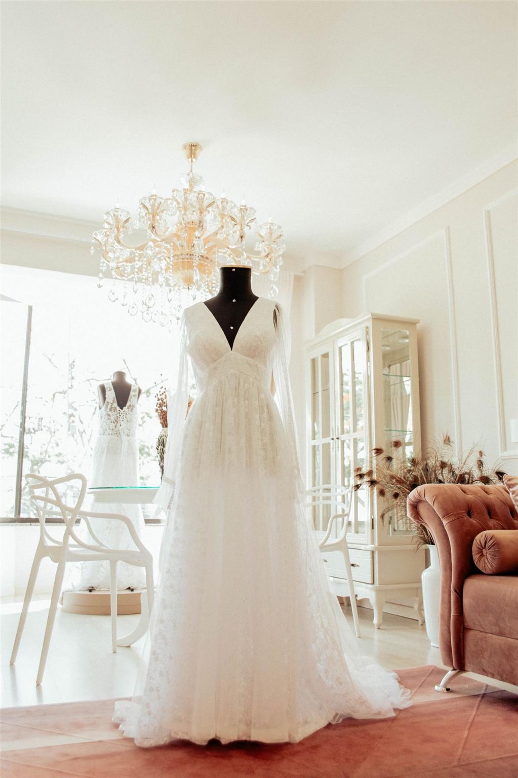 Ein weißes Brautkleid aus Spitze, das auf einem Mannequin in einem eleganten, lichtdurchfluteten Raum präsentiert wird.