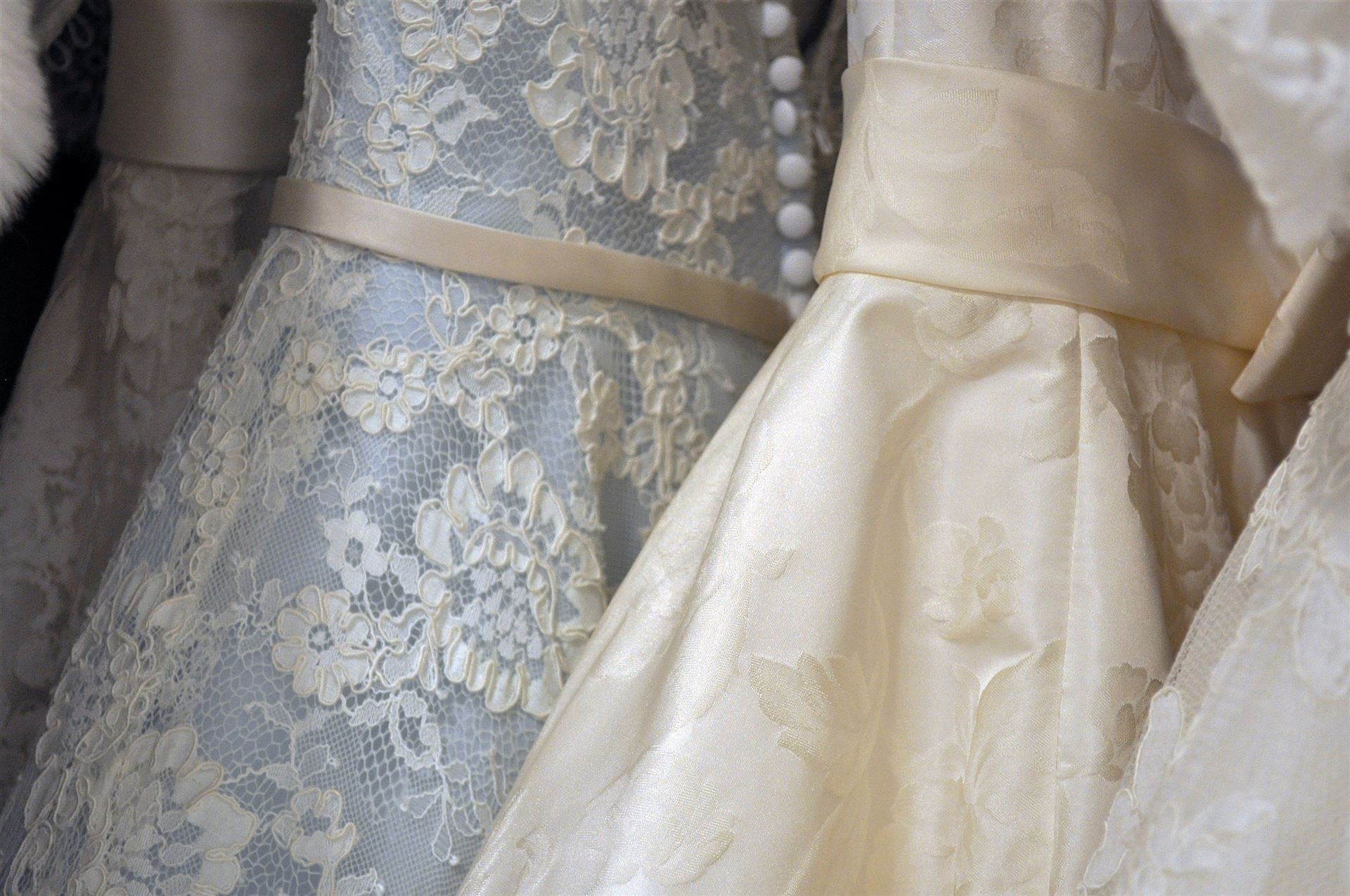Nahaufnahme mehrerer elegante Brautkleider mit Spitze und fließendem Satinstoff.