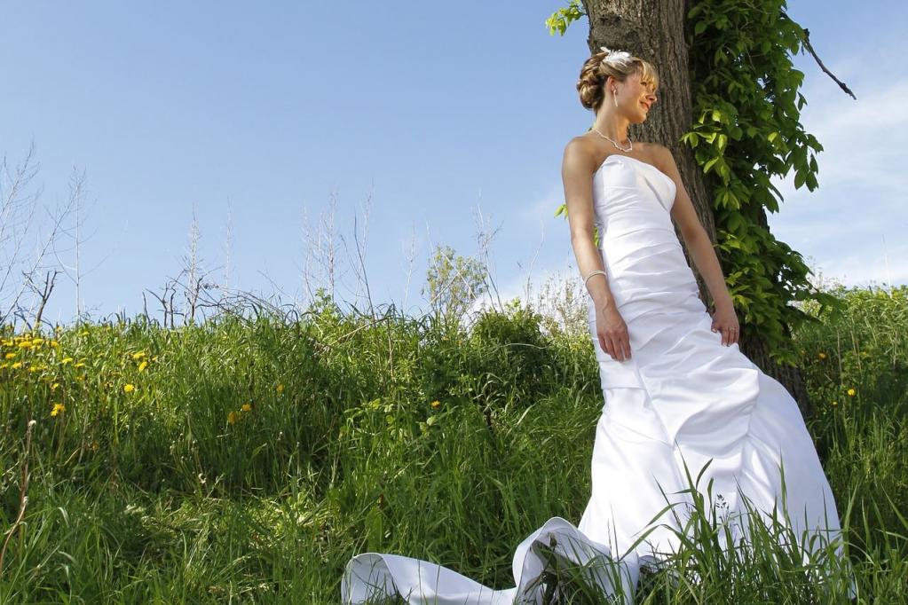 Eine Frau in einem weißen Kleid steht unter einem großen Laubbaum in einem sonnendurchfluteten, grünen Feld.