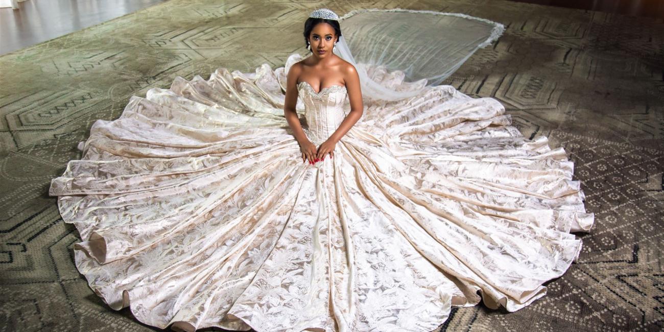 Eine Frau präsentiert ein sehr großes, opulent verziertes Brautkleid mit weit ausgestelltem Rock.