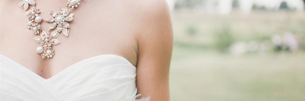 Nahaufnahme des Dekolletés einer Frau in einem weißen, schulterfreien Brautkleid mit einem verzierten, perlenbesetzten Schmuckstück.