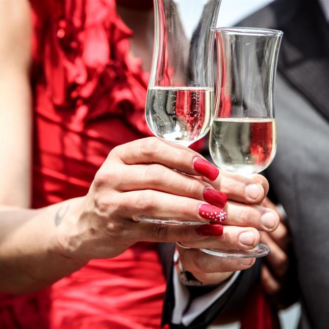 Eine Frau in einem roten Kleid und ein Mann in einem Anzug stoßen bei einem festlichen Anlass mit Gläsern an.