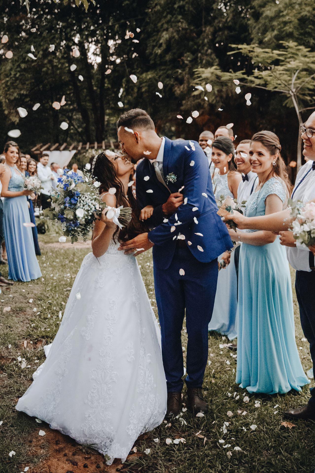 Ein junges Hochzeitspaar küsst sich im Freien, während Blütenblätter herabfallen.