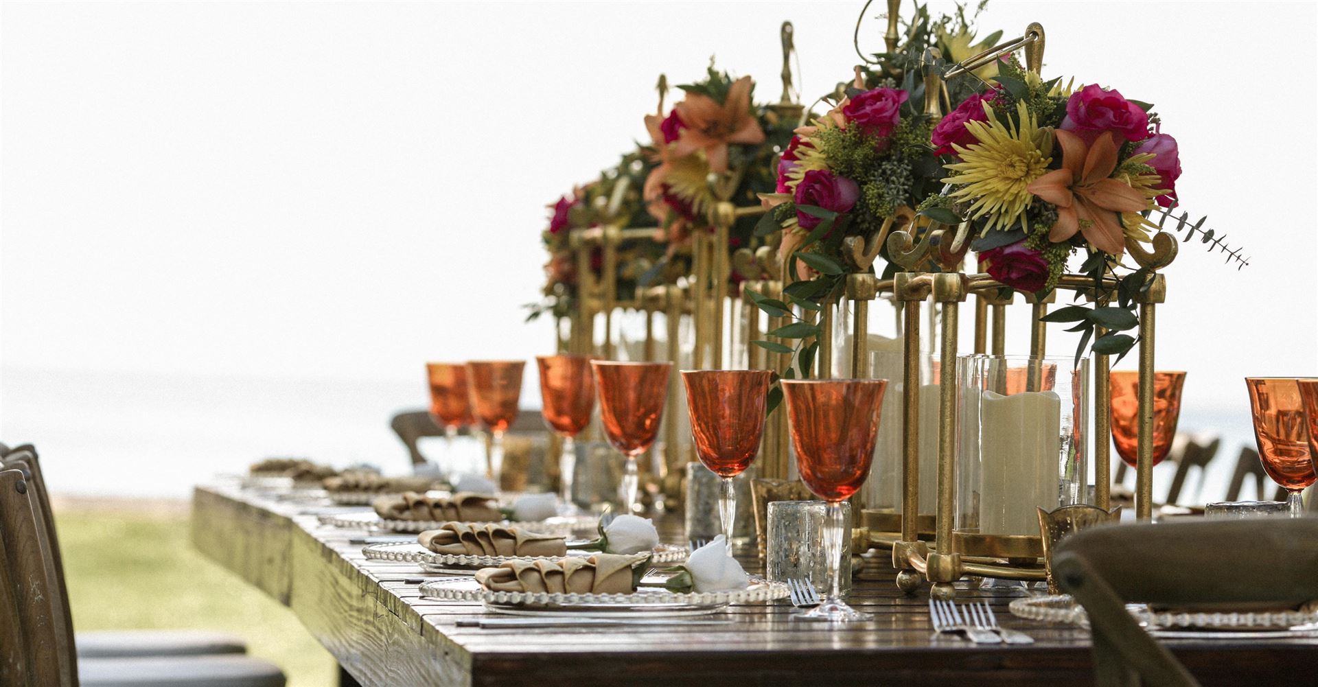 Ein langer Holztisch ist mit opulenten Blumenarrangements und Kerzen für ein festliches Outdoor-Dinner dekoriert.