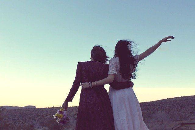 Zwei Frauen stehen auf einer Anhöhe bei Sonnenuntergang und blicken auf eine weite, hügelige Landschaft.