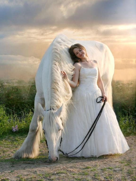 Eine Frau in weißem Kleid steht neben einem weißen Pferd vor einem dramatischen Sonnenuntergang.