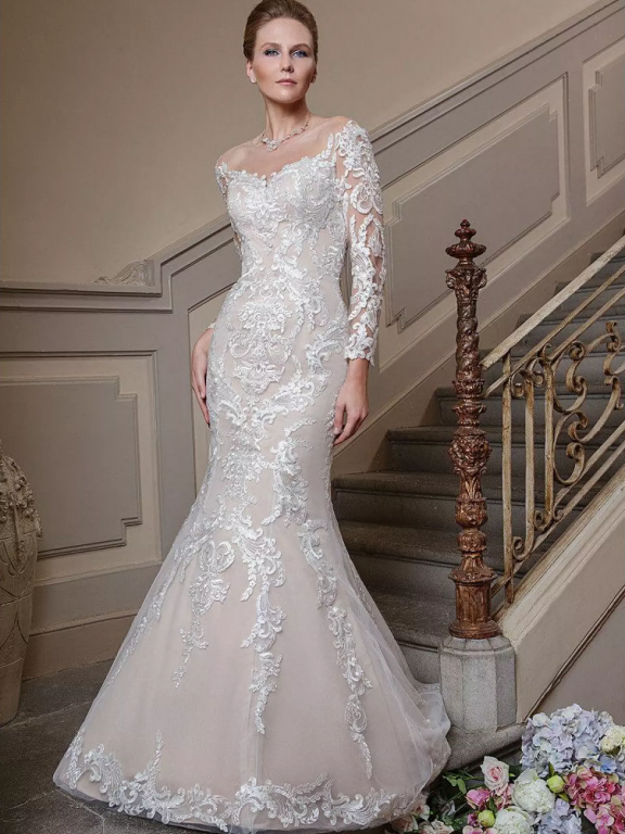 Eine Frau in einem weißen, bestickten Brautkleid posiert an einer verzierten Steintreppe.