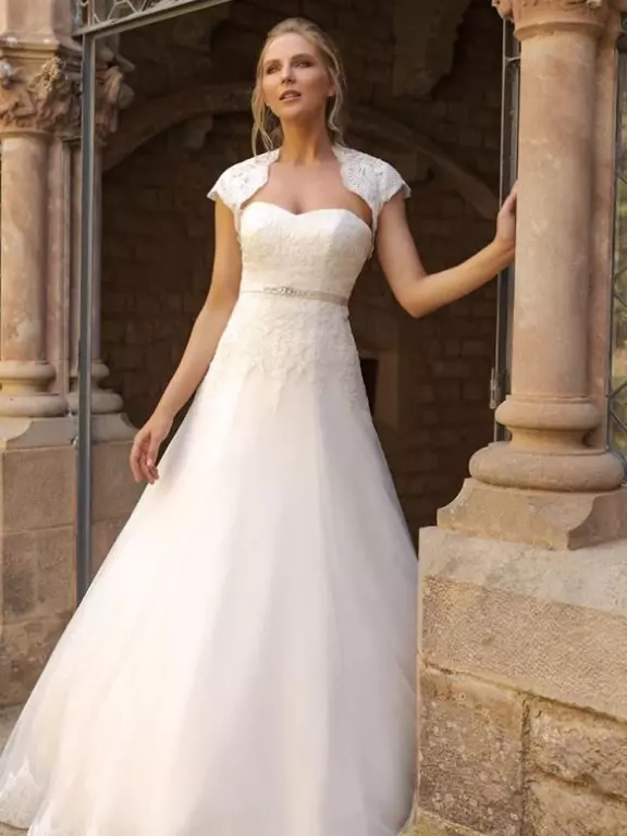Eine blonde Frau in einem eleganten, weißen Hochzeitskleid, die neben klassischen steinernen Säulen posiert.