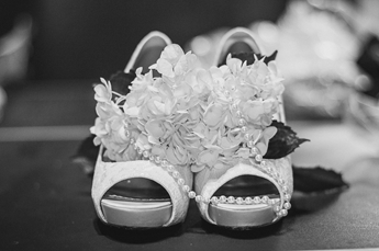 Schwarzweißaufnahme eines Paar Sandalen, die von einem Strauß weißer Blumen umgeben sind.