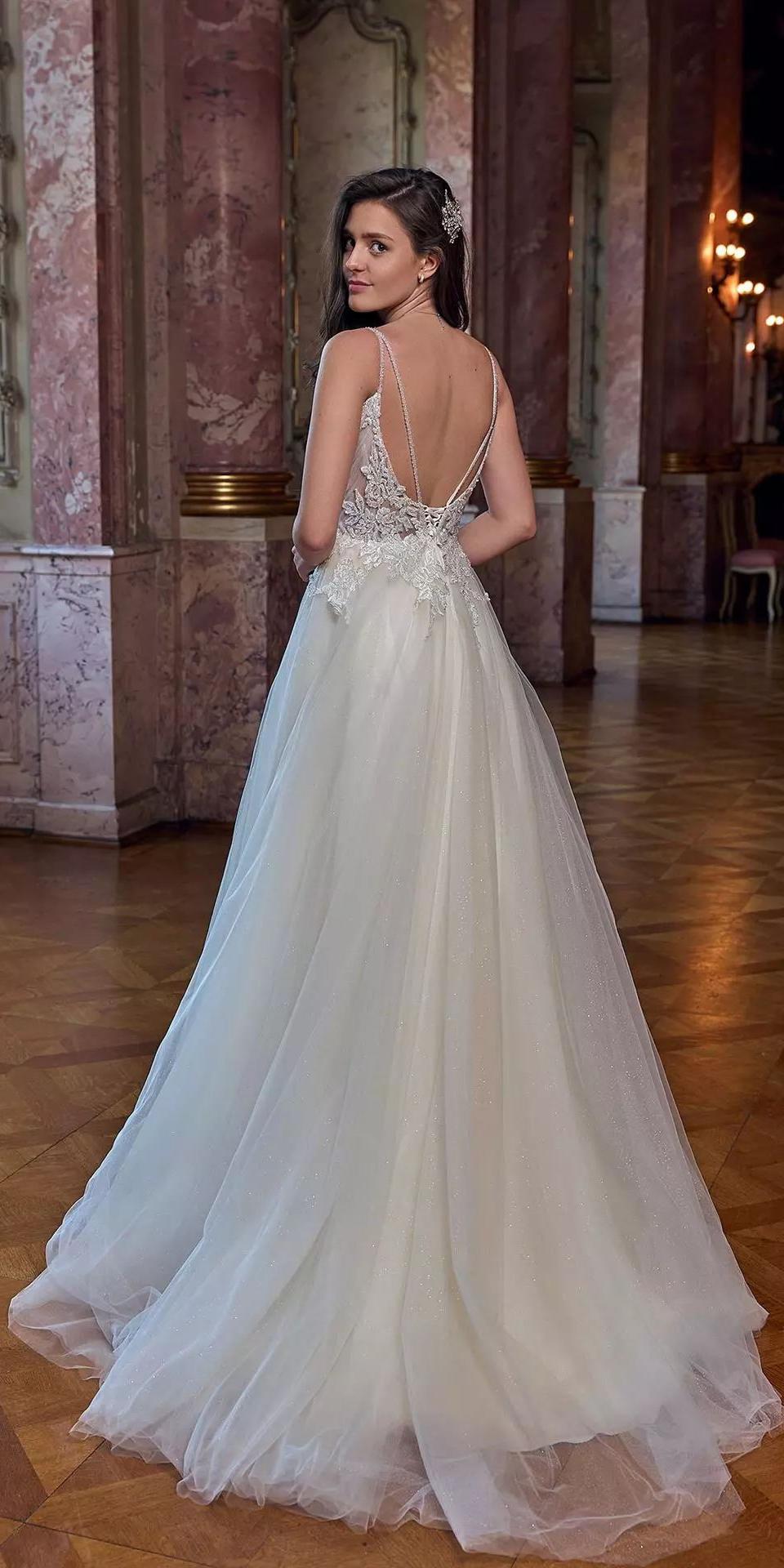 Eine junge Frau in einem weißen, voluminösen Brautkleid steht in einem historischen und prunkvollen Saal.