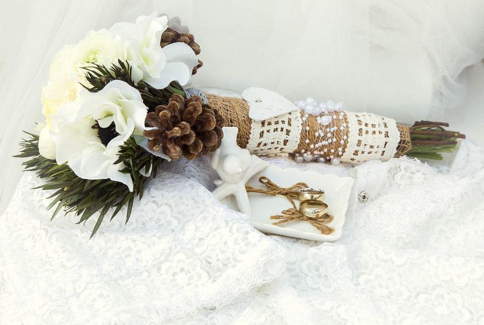 Flatlay mit weißen Blumenstrauß, Tannenzapfen, Muschelschale und rustikalen Hochzeitsaccessoires auf weißem Tüll.
